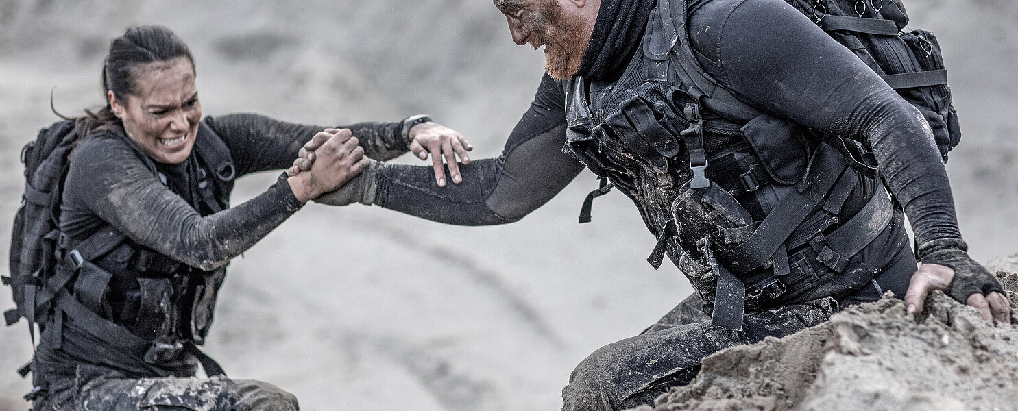 Redhead male and brunette female military members training hard and helping each other on a sand hill run
