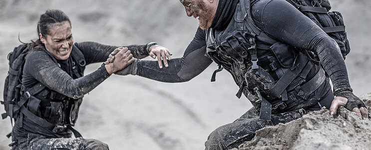 Redhead male and brunette female military members training hard and helping each other on a sand hill run